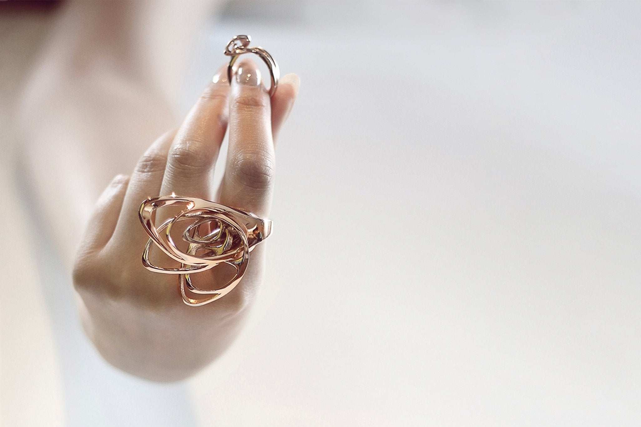 Hand wearing rose gold sculptural rings holding a smaller ring, COVID-19 LACE Update jewelry piece.