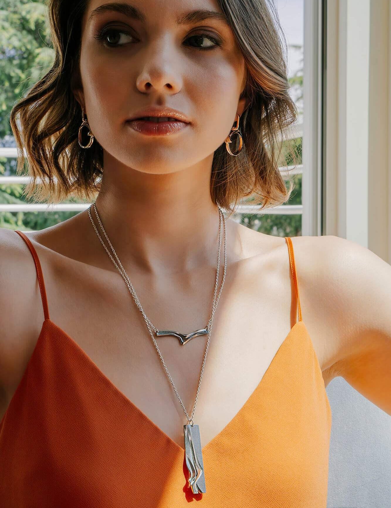 Andante Stainless Steel Pendant with twisting stacking curves worn by woman in orange dress
