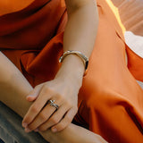 Close-up of a hand wearing an Oblique Cuff bracelet in sterling silver, styled with an orange satin dress.