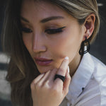 Close-up of woman wearing Aura Carbon lightweight black carbon fiber earrings with misaligned loops and matching ring