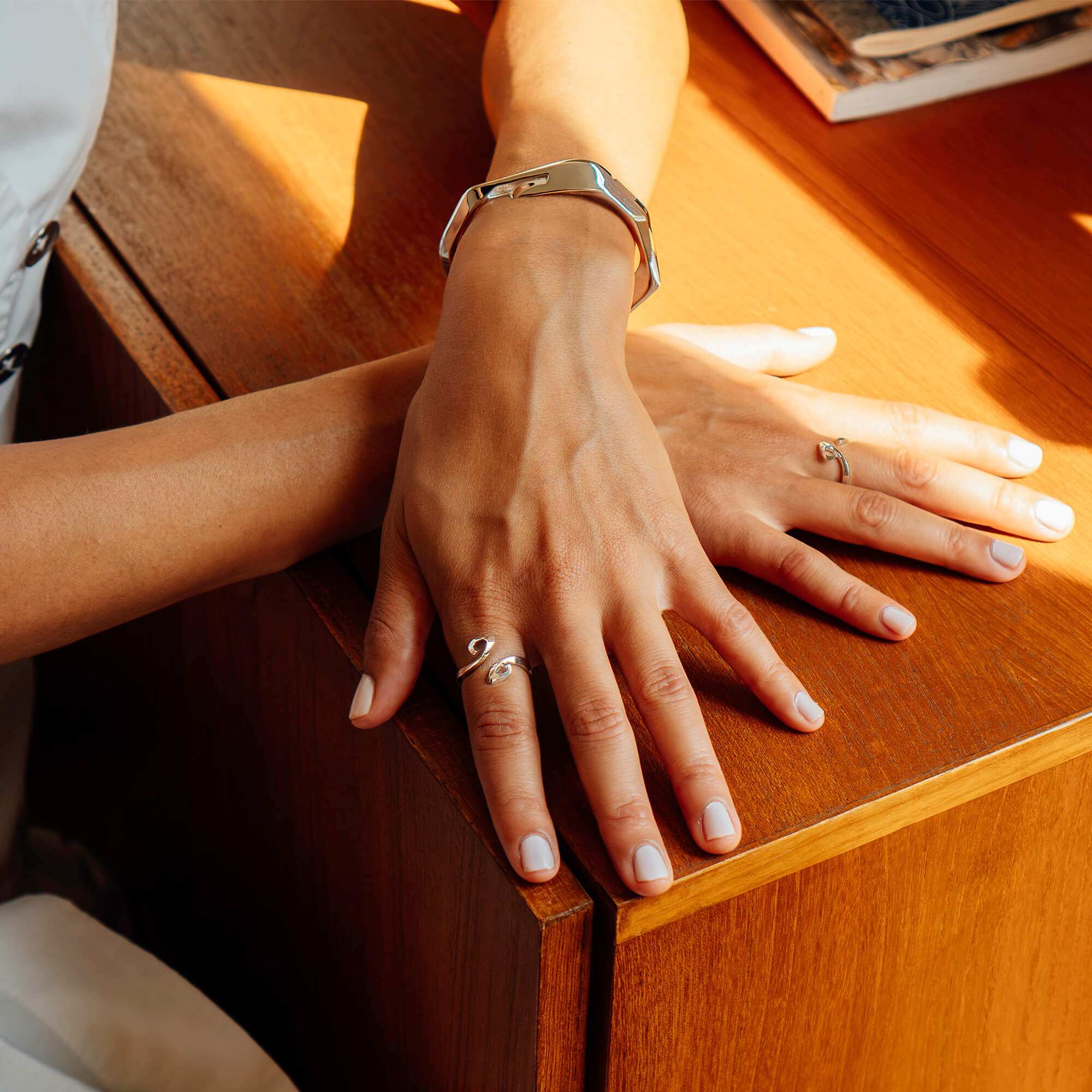 Hydra Duo ring in sterling silver on a hand with a silver bracelet on wooden table in natural light