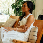 Woman wearing white dress sitting on chair showcasing Hydra Ring on finger with natural indoor background