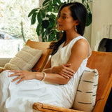 Woman wearing white dress sitting on chair showcasing Hydra Ring on finger with natural indoor background