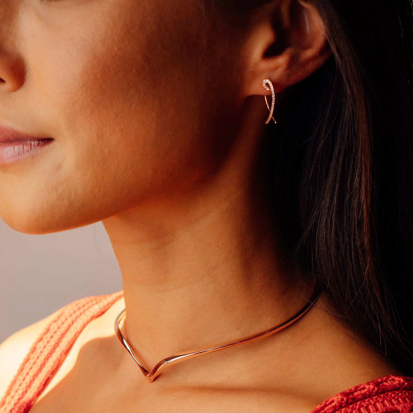 Close-up of a woman wearing elegant Hydra diamond earrings with intertwined looped design in 14K gold, featuring sparkling 0.11ct diamonds.