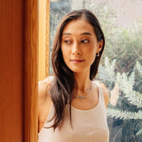 Woman wearing Calyx Mini Hoop silver earrings looking out window with plants in background