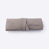 Gray travel jewelry roll organizer made of soft microfiber material, rolled and secured with a strap.