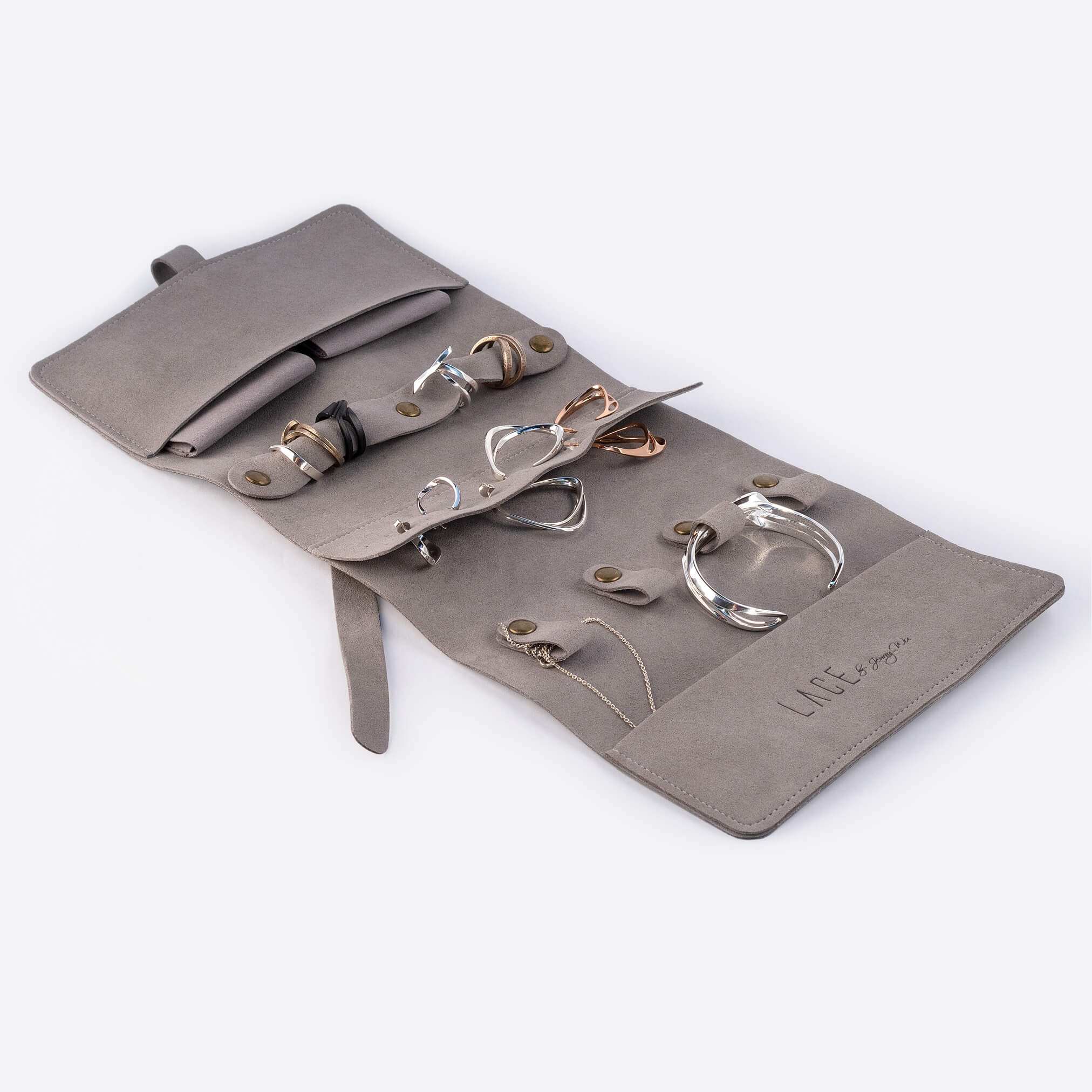 Gray microfiber travel jewelry roll organizer with multiple compartments and various jewelry pieces inside