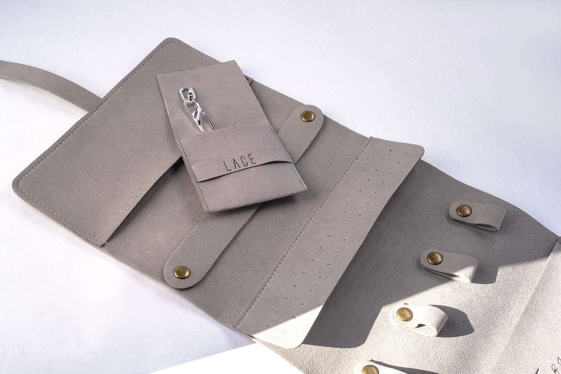 Gray microfiber travel jewelry roll with multiple compartments and small pouch for organizing jewelry.