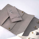 Gray microfiber travel jewelry roll with multiple compartments and small pouch for organizing jewelry.