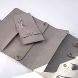 Gray microfiber travel jewelry roll with multiple compartments and small pouch for organizing jewelry.