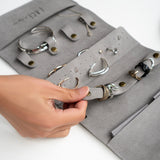 Gray travel jewelry roll organizer made of soft microfiber with compartments for rings, earrings, and bracelets.