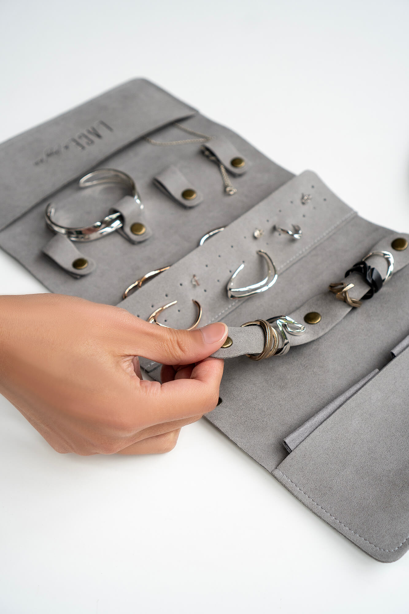 Gray travel jewelry roll organizer made of soft microfiber with compartments for rings, earrings, and bracelets.
