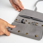 Gray travel jewelry roll organizer made of soft microfiber with compartments for rings and earrings, held by hands on white background