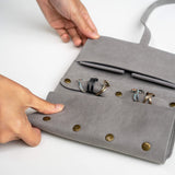 Gray travel jewelry roll organizer made of soft microfiber with compartments for rings and earrings, held by hands on white background