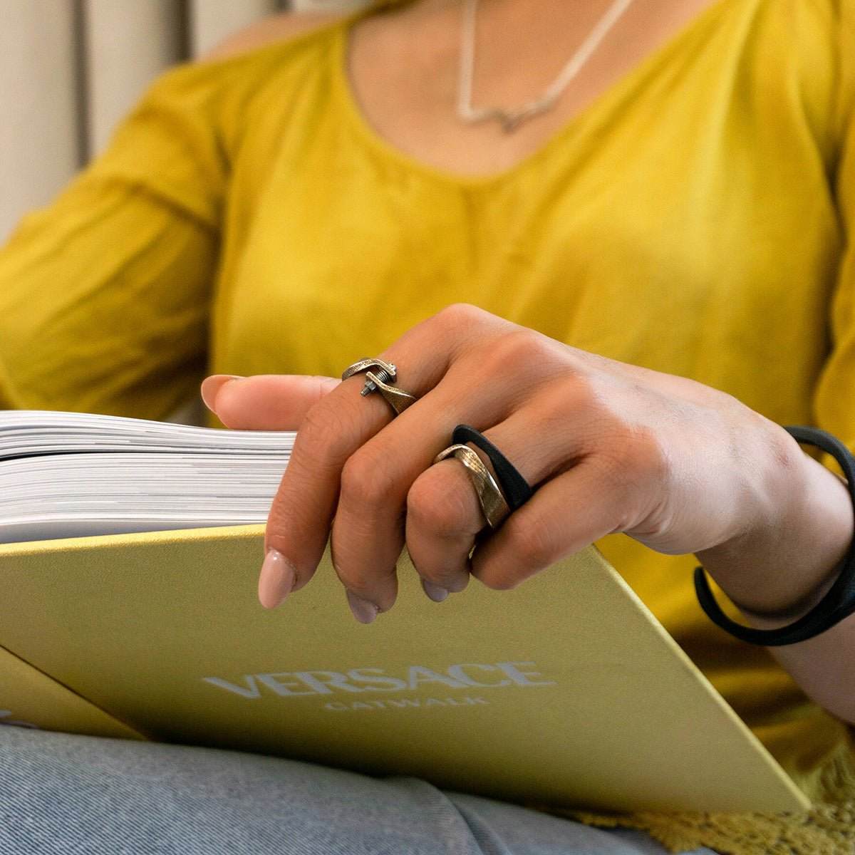 Close-up of hand wearing Amos Steel Ring and reading a Versace book
