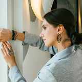 Woman wearing Eclipse Carbon Earrings with overlapping oval ring design in carbon fiber near a wall with reflective surface