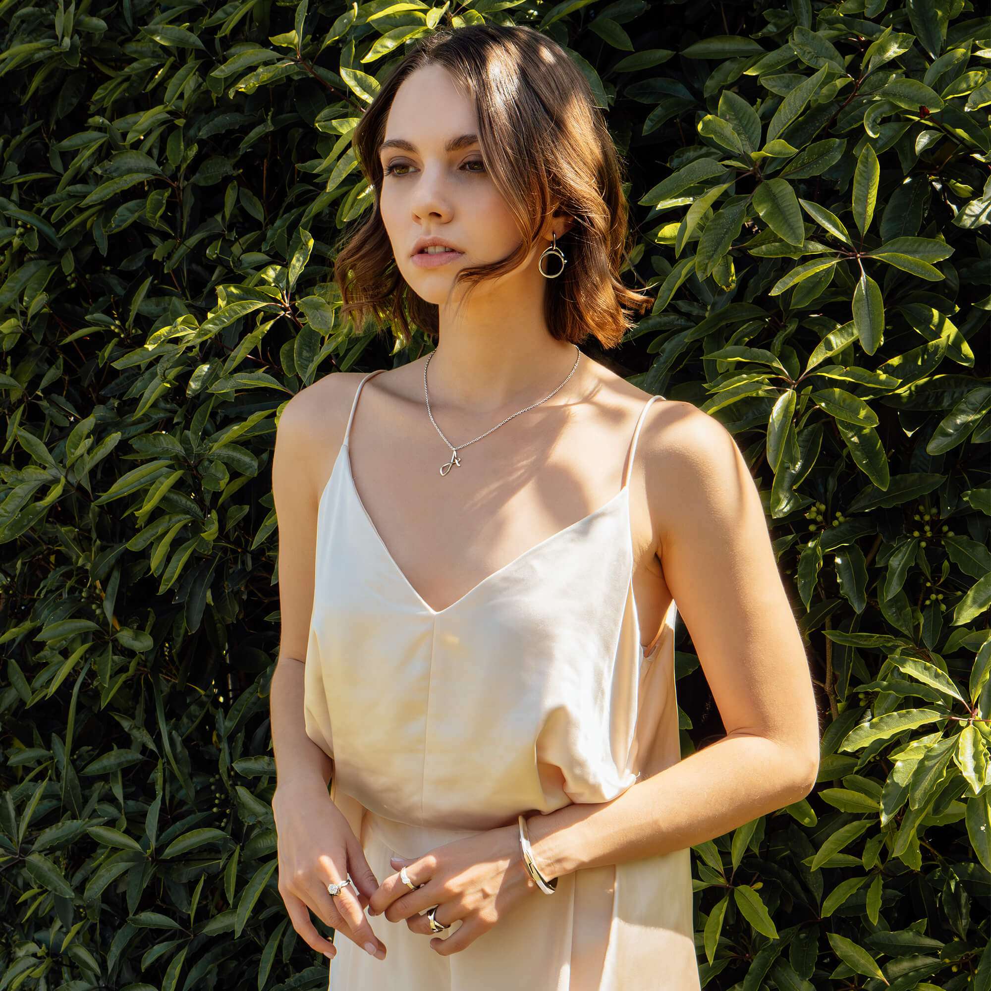 Woman wearing a delicate initials pendant necklace with three-dimensional script on a thin chain, styled as an elegant layering piece