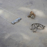 Adagio Stainless Steel Pendant with twisting, stacking curves on a chain displayed on a concrete surface
