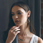 Woman wearing Aura Steel earrings with two slightly angled stainless steel loops and matching silver jewelry