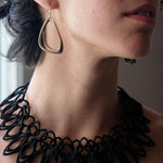 Aura Steel stainless steel misaligned loop hoop earring worn by woman with black necklace