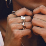 Close-up of hands wearing stackable Amor Amos Light Set rings with twisting band and edge detailing in sterling silver