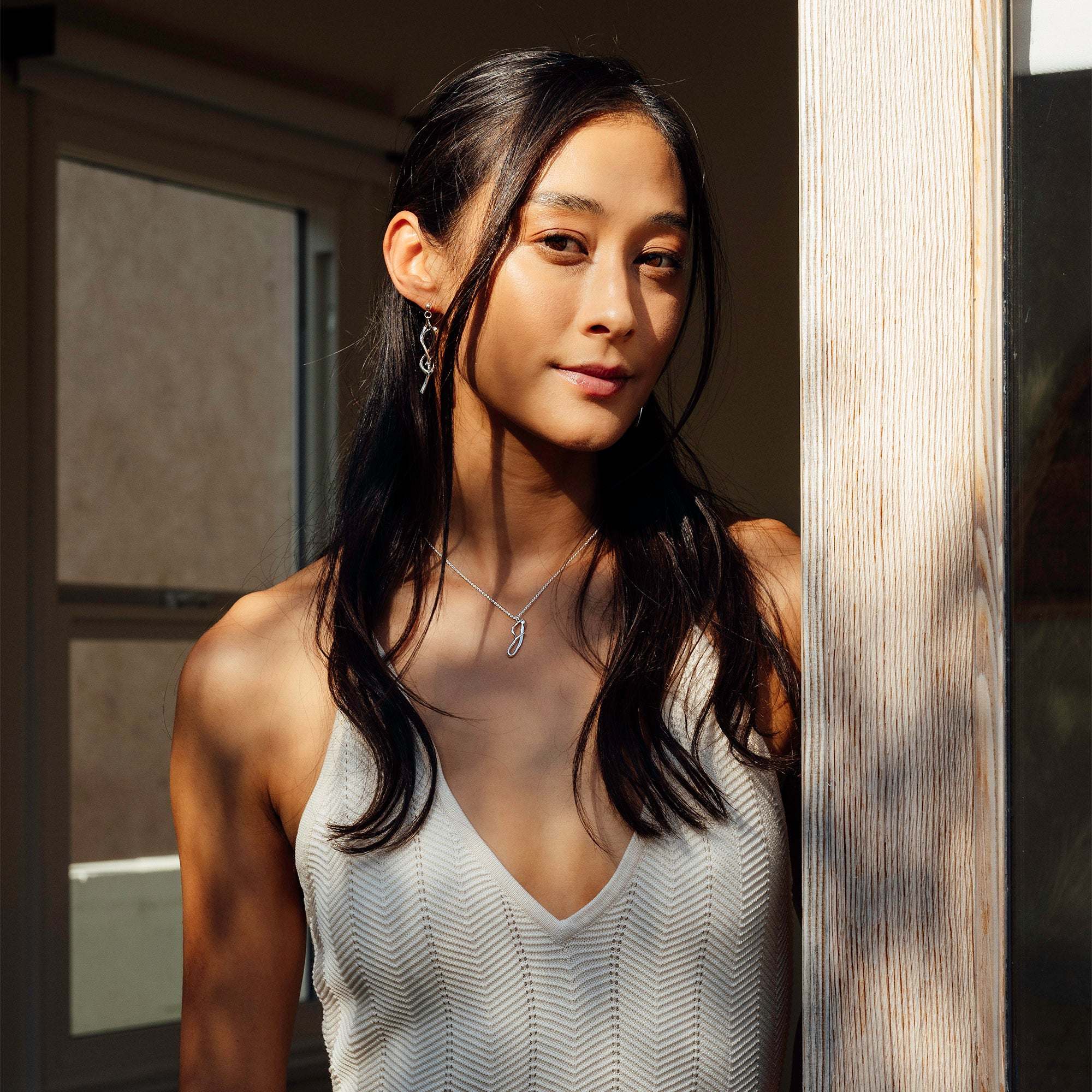 Woman wearing elegant Nova earrings with a delicate undulating curve and knot design in natural light