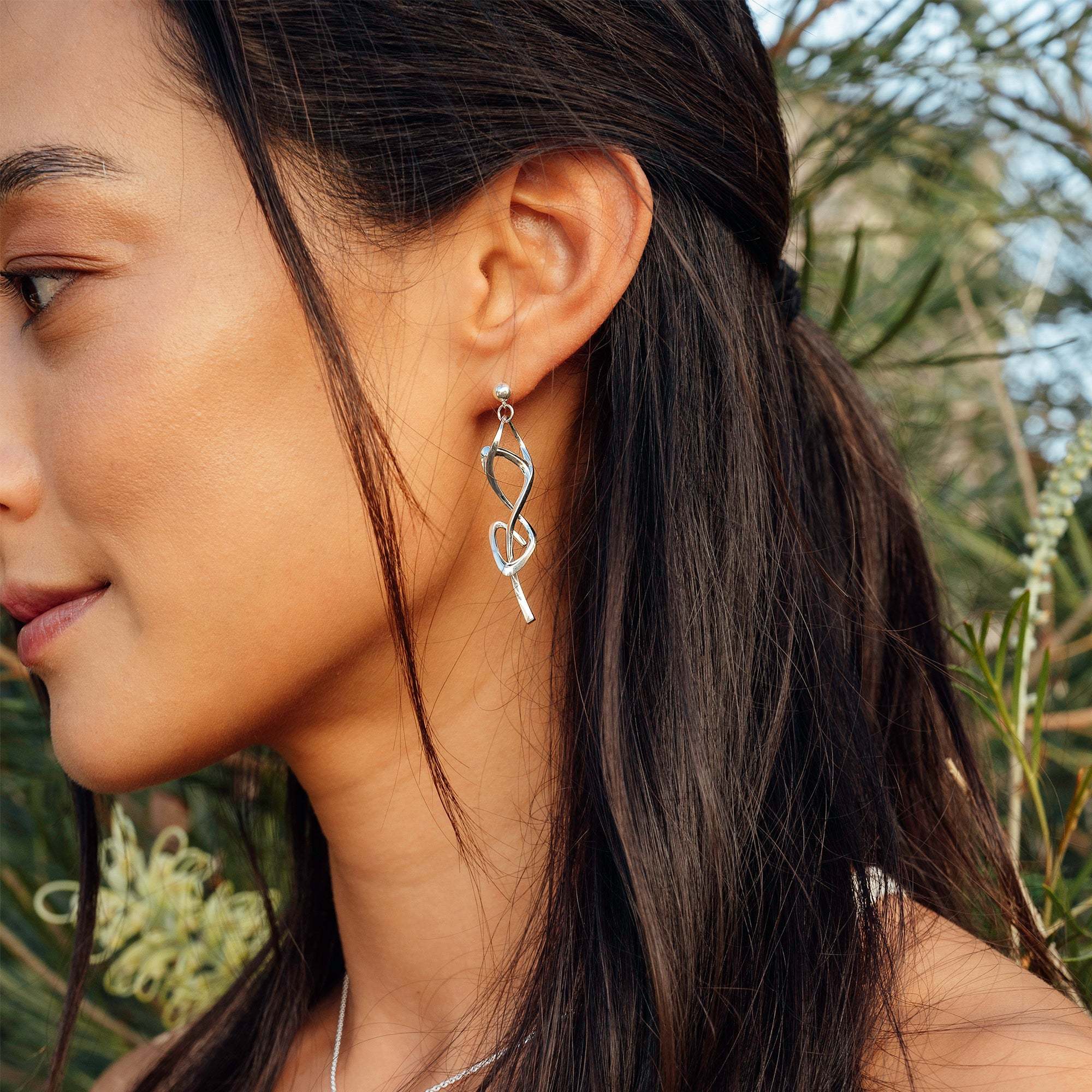 Woman wearing Nova earrings in sterling silver with elegant undulating curve and loose knot design
