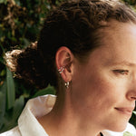 Close-up of a woman wearing Linea Earrings Set including a twisting band ear cuff and mini hoop earrings in sterling silver