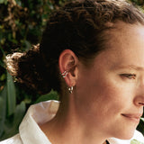 Close-up of a woman wearing Linea Earrings Set including a twisting band ear cuff and mini hoop earrings in sterling silver