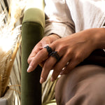 Close-up of hand wearing three black nylon ring samples from Lace collection, resting on green armchair with soft natural light