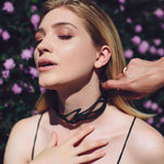 Woman wearing Legato black 3D printed flexible TPU choker necklace with twisting, stacking curves and precision edge detailing outdoors with purple flowers background