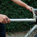 Man wearing Amor Bold Steel Ring on hand while holding a silver bicycle frame outdoors