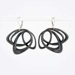 Pair of black steel Gemino earrings with interlocking elliptical petals design hanging on a white rod