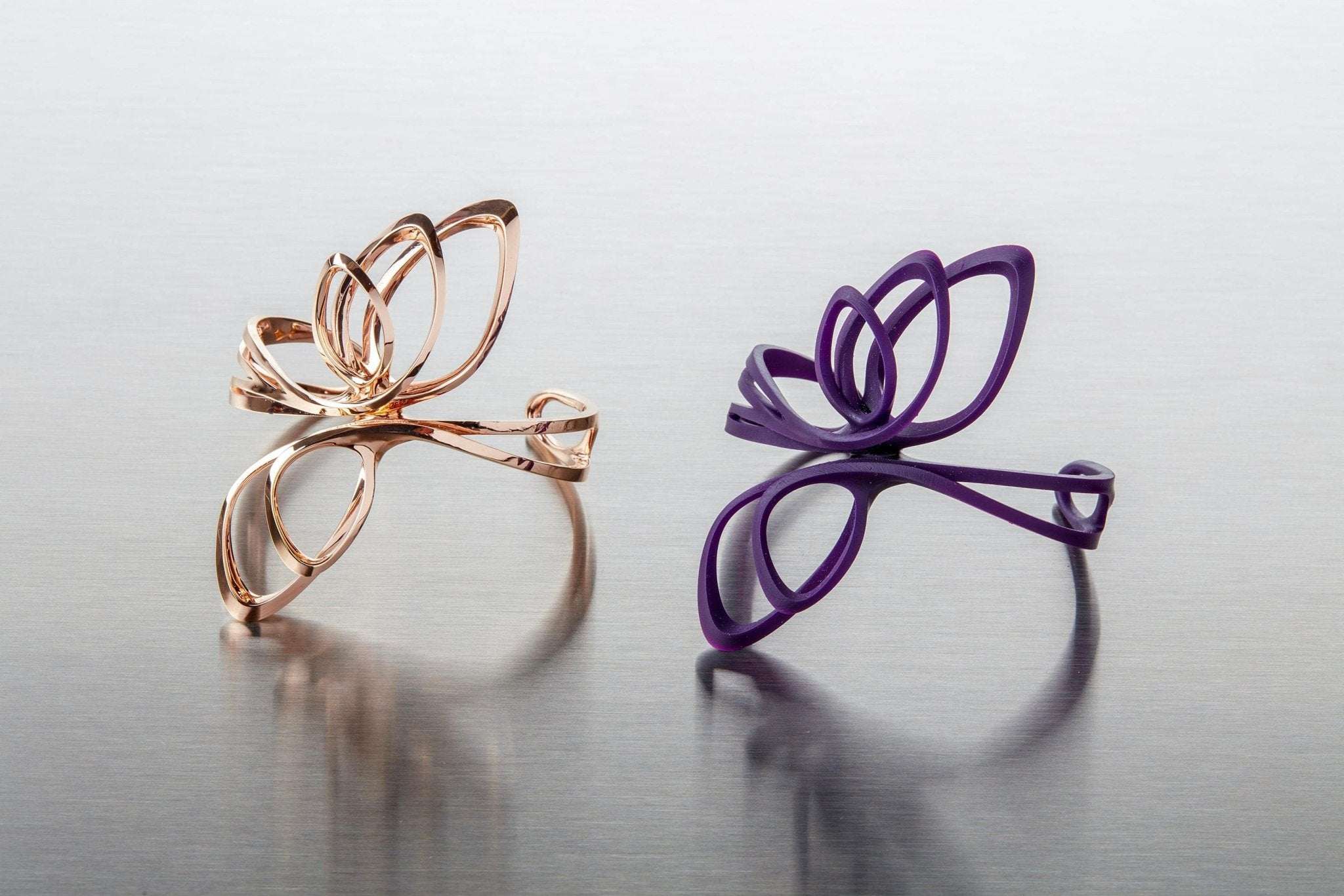 Rose gold and purple 3D printed butterfly-shaped bracelets on reflective surface showcasing 3D printing technologies in jewelry.