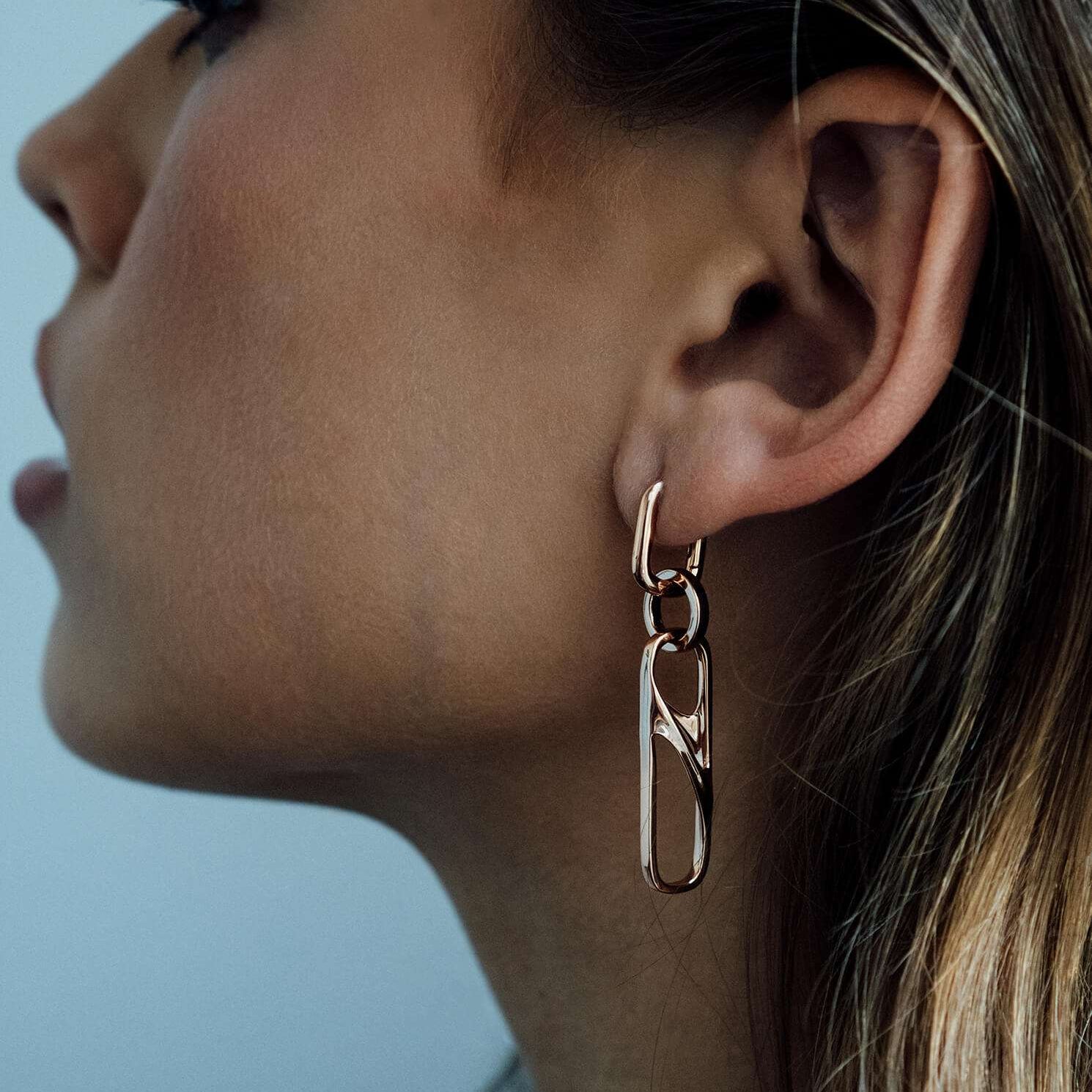 Close-up of a woman wearing a gold chain earring with three linked rectangular shapes, showcasing elegant dangle design.