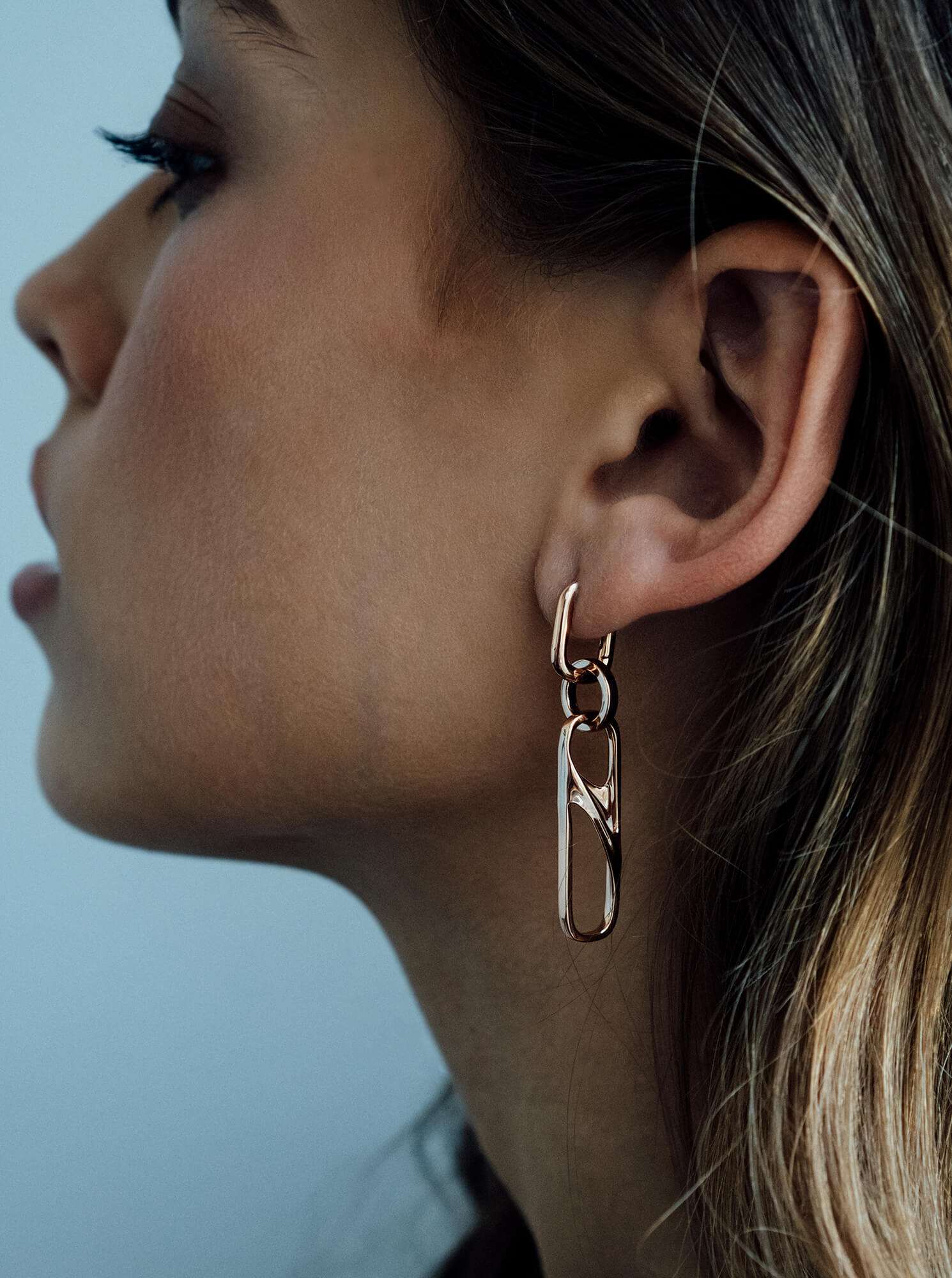 Close-up of a woman wearing a gold chain earring with three linked rectangular shapes, showcasing elegant dangle design.