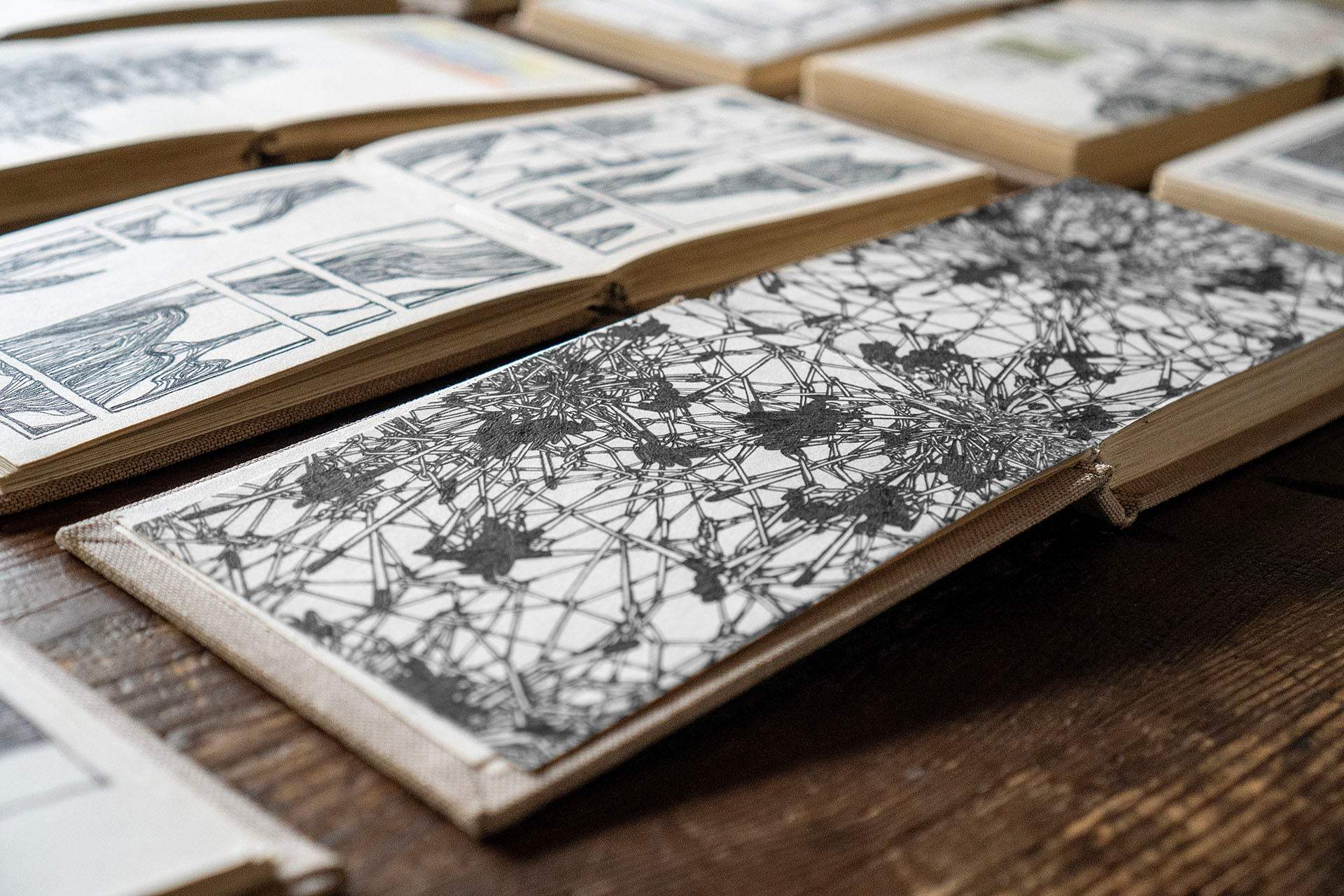 linen covered sketchbook open to detailed black ink sketches on wooden table showcasing unique sketchbook design