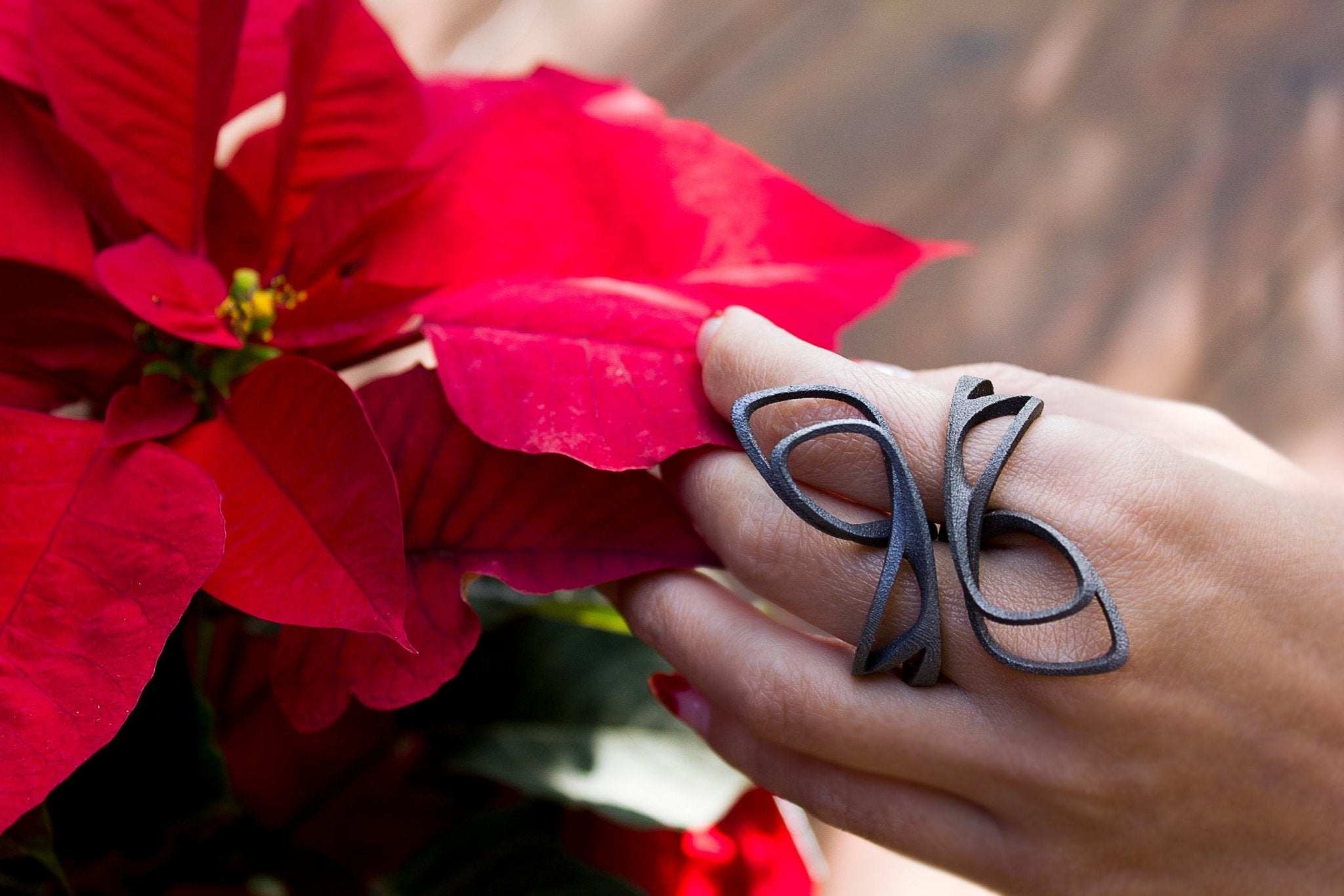 Hand wearing black butterfly ring holding red poinsettia flower symbolizing 2020 holiday deadlines