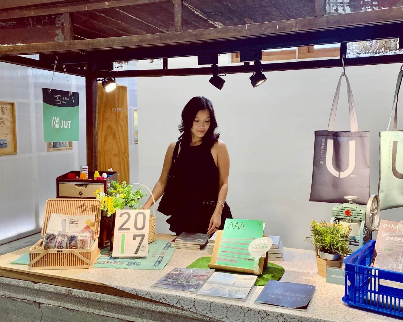Woman standing at a market stall with books, plants, and tote bags under wooden beams, reflecting End of Year 2021 Reflections theme