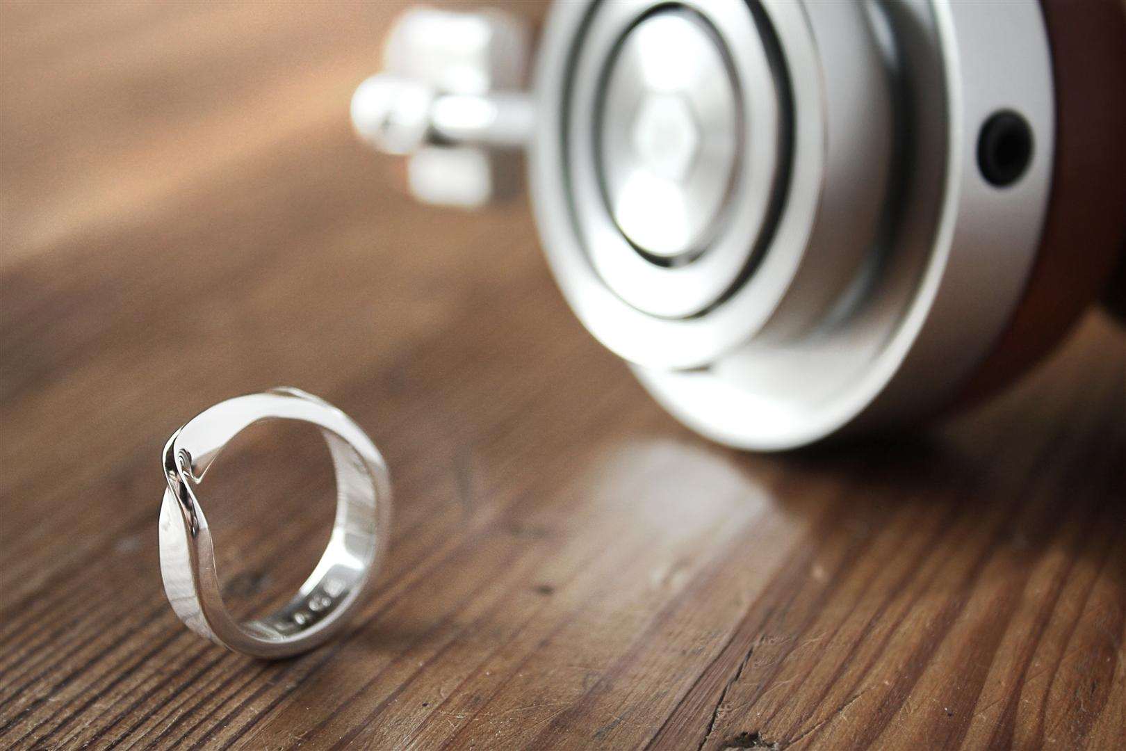 Silver modern minimalist ring on wooden surface with blurred metallic object in background for gift ideas for graduates