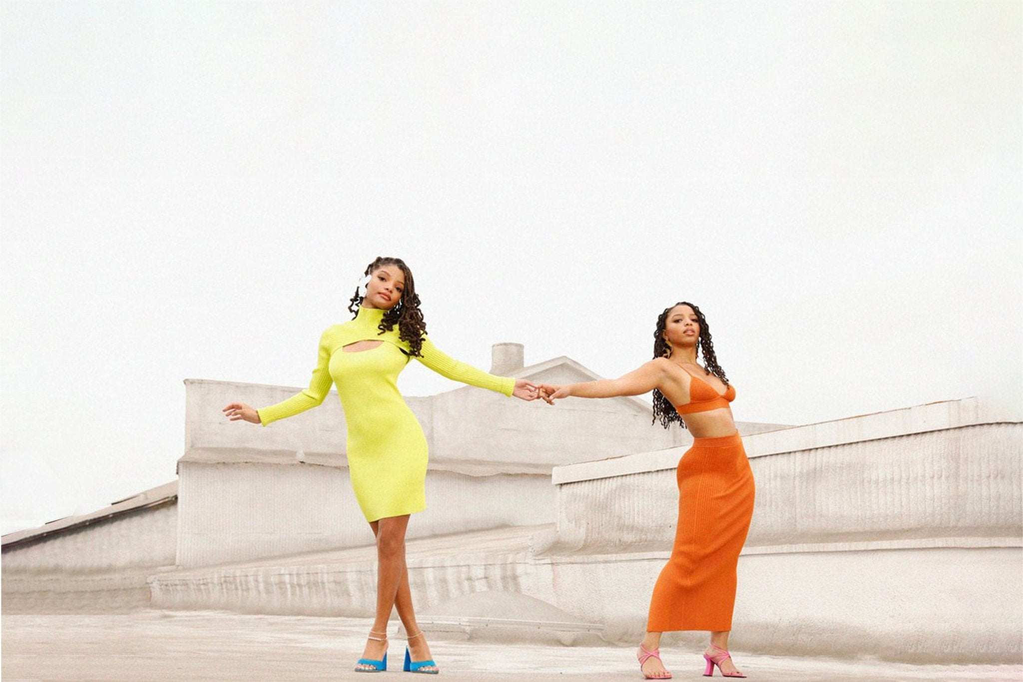 Chloe X Halle sisters posing on rooftop in yellow and orange outfits holding hands
