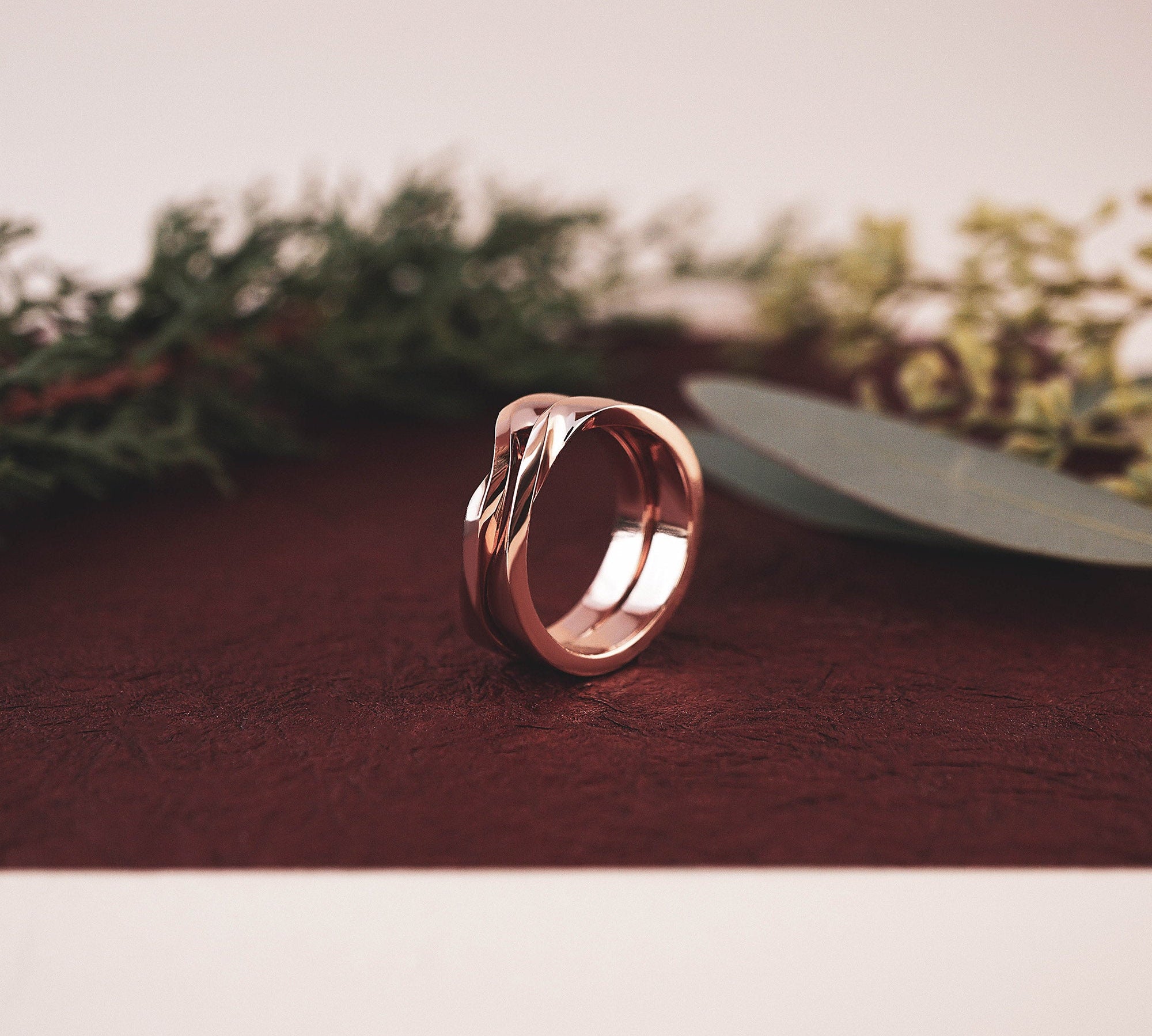 Rose gold Amor Amos Light Set stackable twisting band ring on brown surface with greenery background