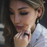 Close-up of woman wearing Aura Carbon lightweight black carbon fiber earrings with misaligned loops and matching ring