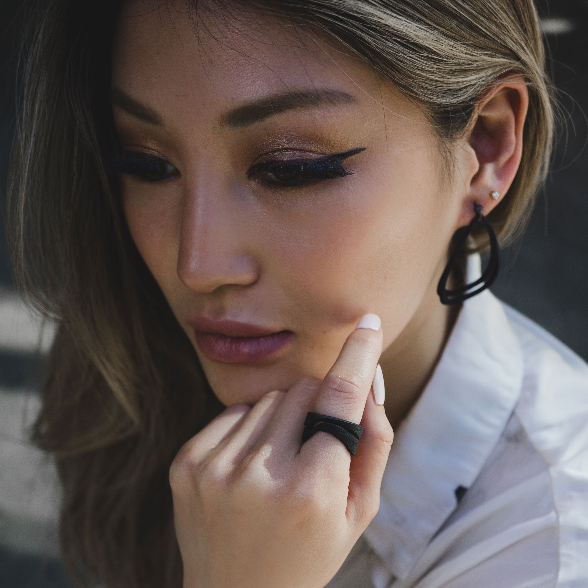 Close-up of woman wearing Aura Carbon lightweight black carbon fiber earrings with misaligned loops and matching ring