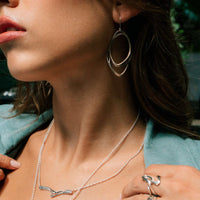 Close-up of woman wearing Eclipse Steel light oval hoop earrings with matching silver necklace and ring