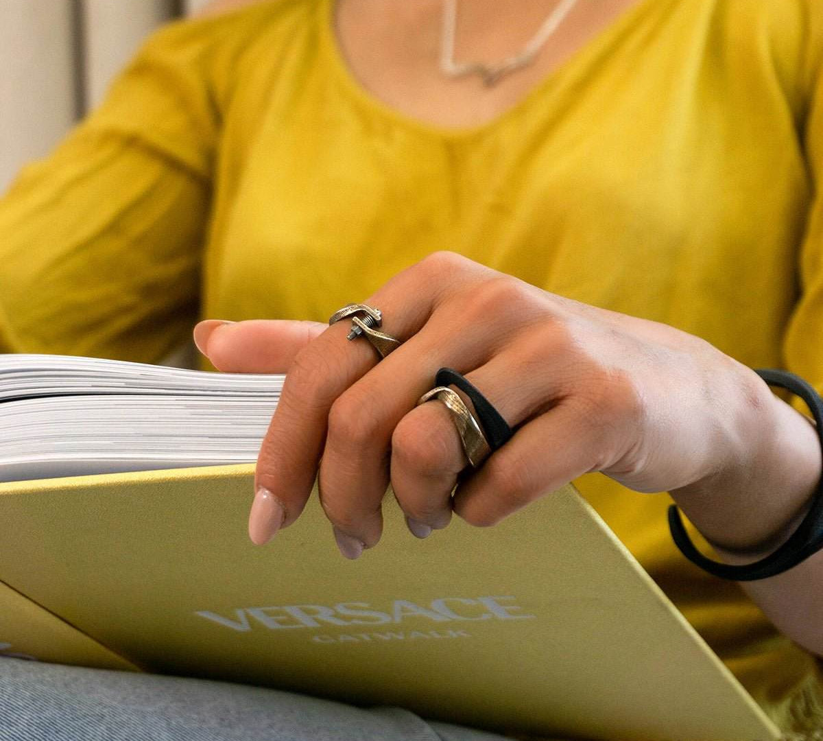 Close-up of hand wearing Amos Steel Ring and reading a Versace book