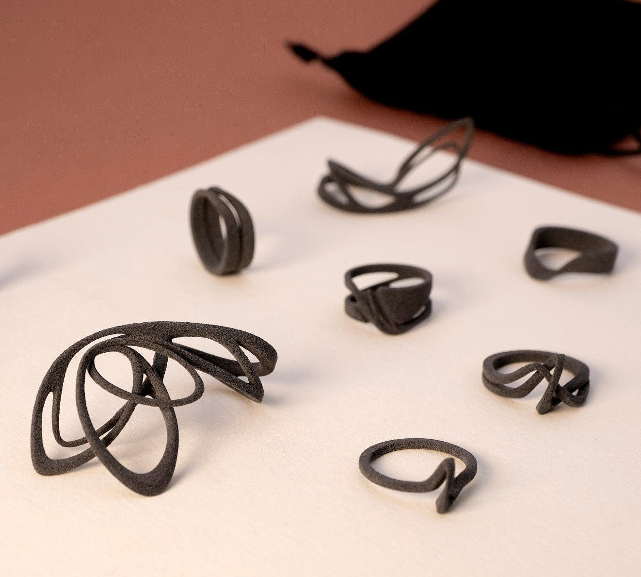 Black nylon ring samples from the LACE collection displayed on white surface with velvet pouch in background