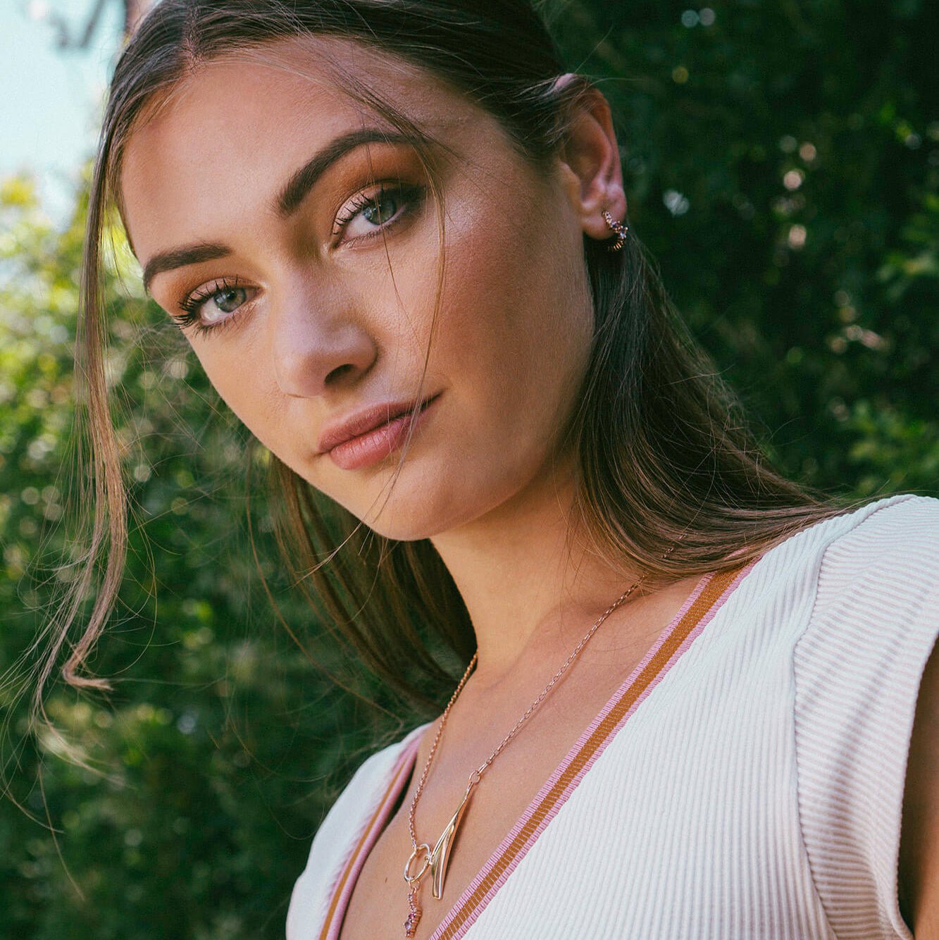 Close-up of woman wearing Leda Earrings with lilac and pink gemstones in 18K rose gold vermeil against green outdoor background