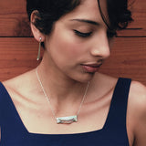 Woman wearing Adagio Velum Set sterling silver pendant and matching earring against wooden background