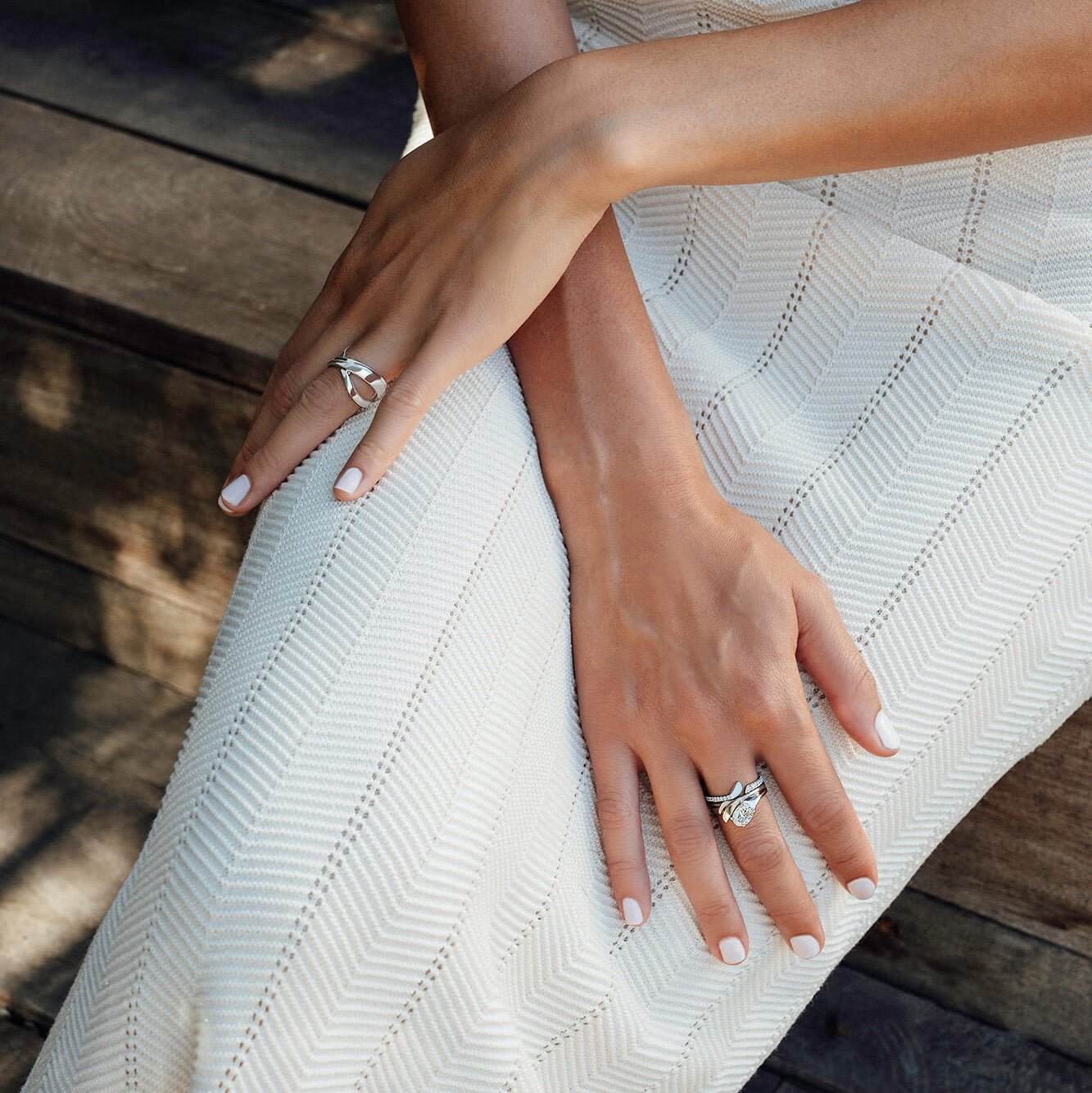 Rosae Wedding Band on woman's hand with sculpted petal design, worn on white dress background